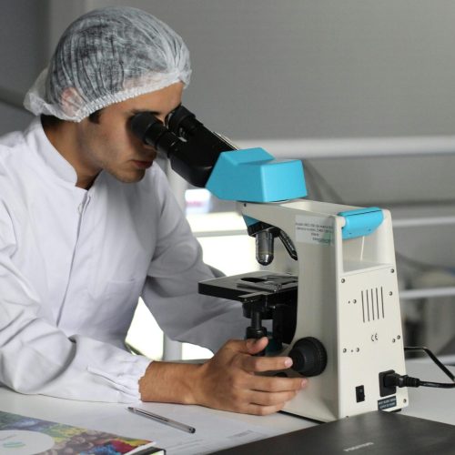 Scientist in a lab coat using a microscope to conduct research, focusing on healthcare improvements.